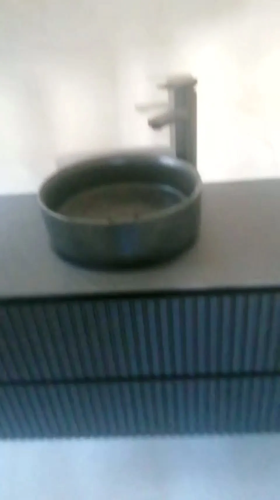 Lavabo redondo de sobre encimera en gris piedra, con grifo alto, sobre un mueble suspendido ranurado
