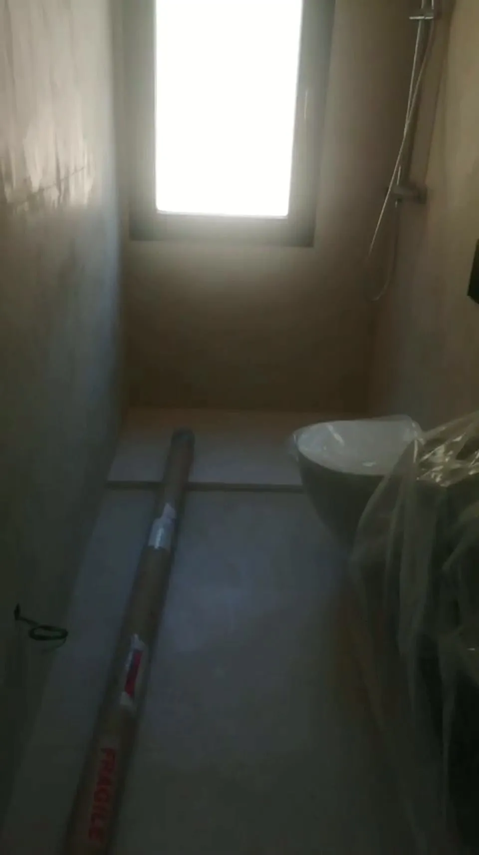 Baño en obra con ventana, inodoro suspendido y ducha, con los muebles aún embalados